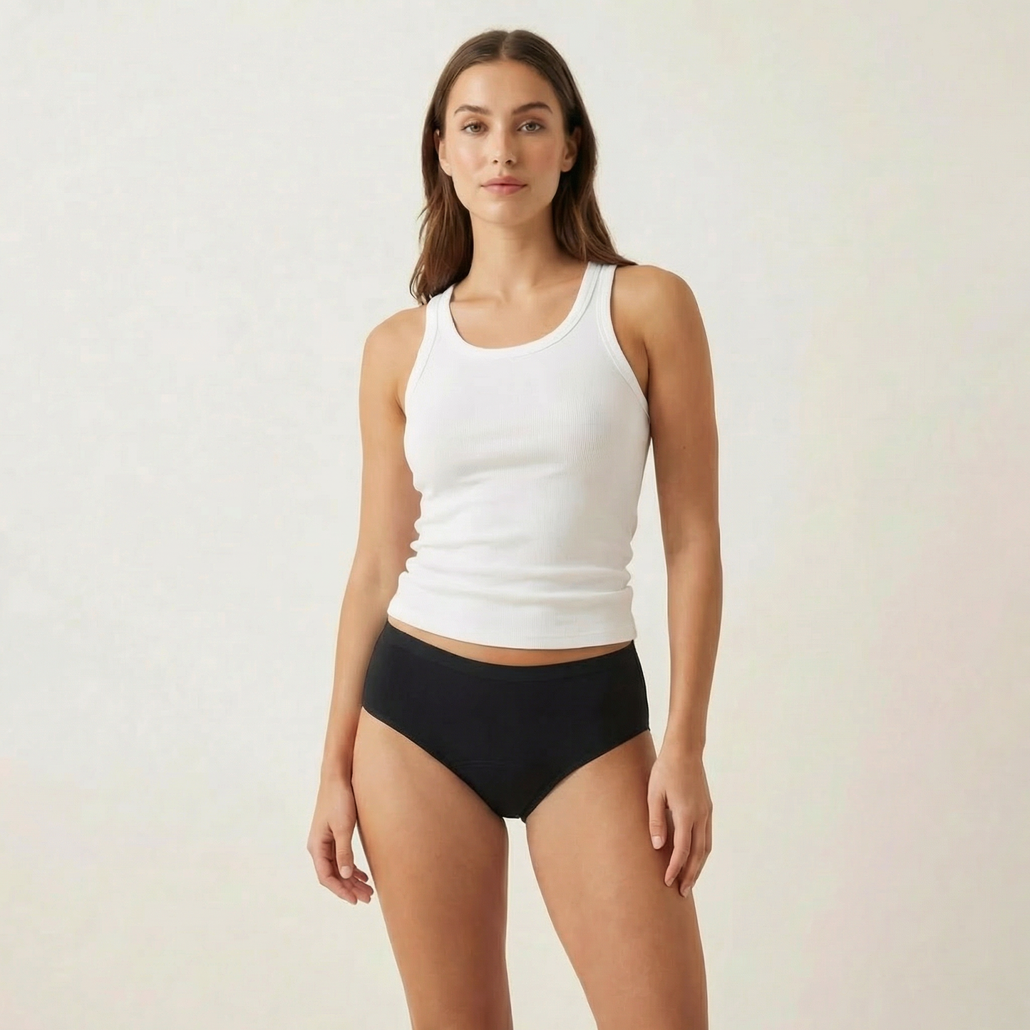Woman wearing a white tank top and black underwear on a plain background